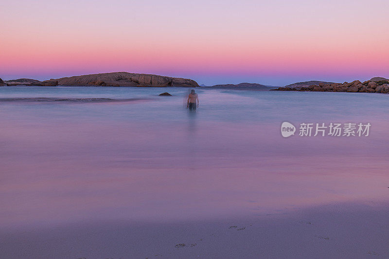 抽象场景的人站在平静的海洋在黄昏反映出柔和的粉红色天空