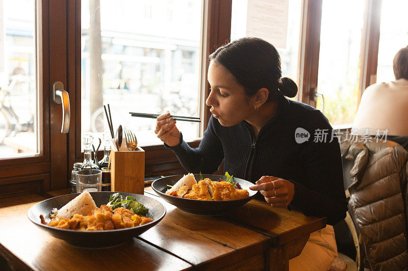 年轻女子在餐厅里吃着越南菜，配上蔬菜、鸡肉和咖喱酱米饭