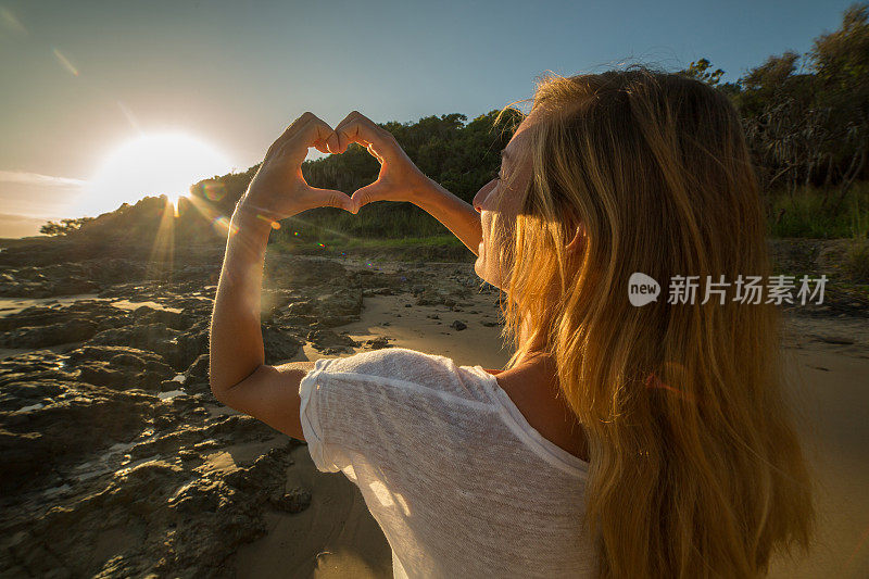 女性框架在海滩上日落成心的形状