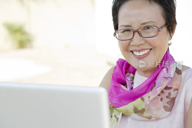 快乐的亚洲资深女性坐在笔记本电脑后面