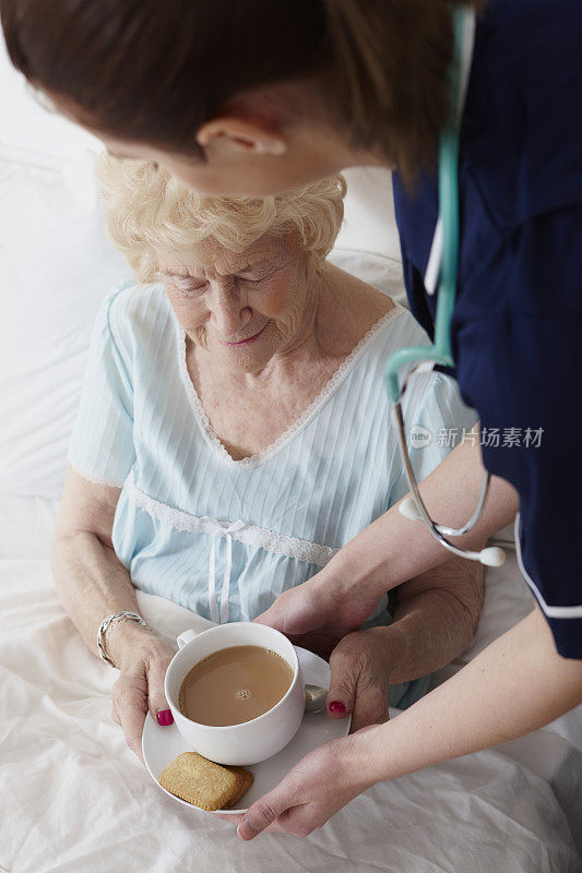 护士在床上给老年妇女倒了一杯茶