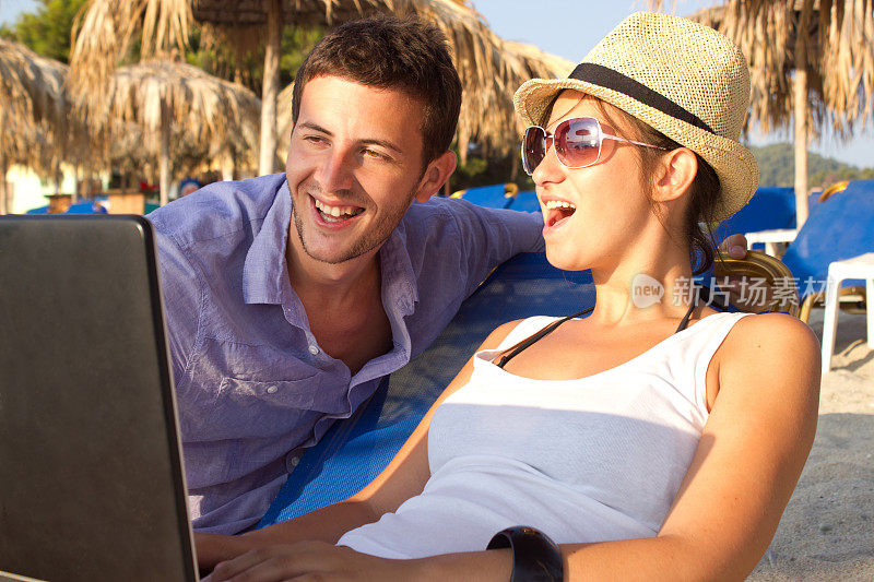 一对年轻的夫妇在沙滩上带着笔记本电脑