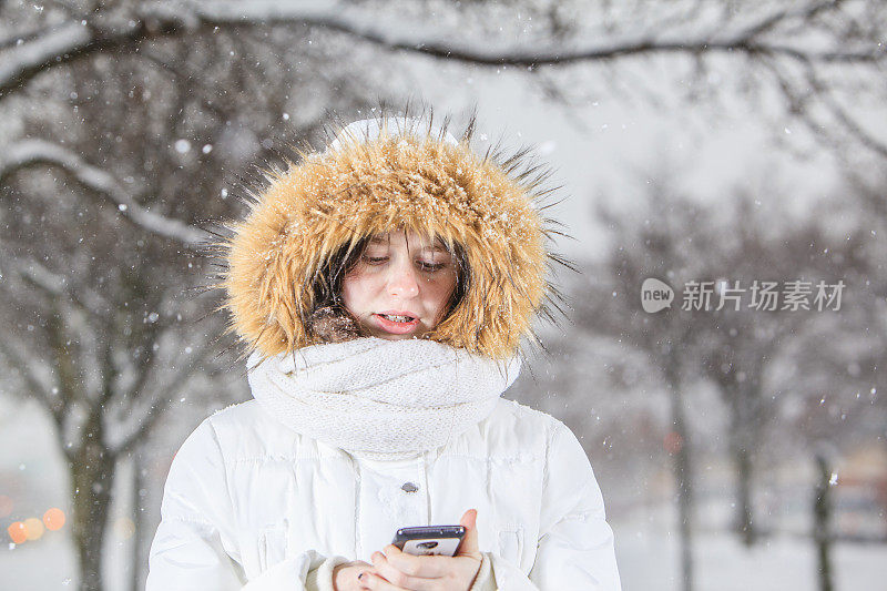 漂亮的少女在下雪的时候用智能手机发短信