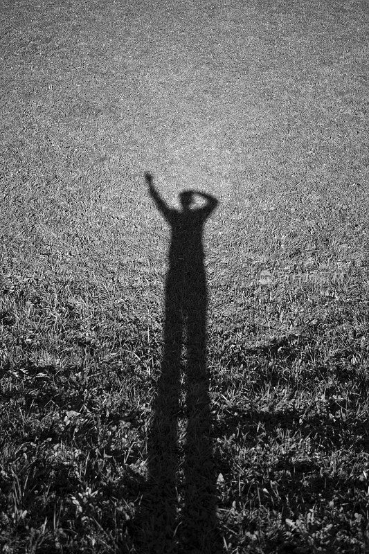 草地上一个挥舞着手的人的影子-单色