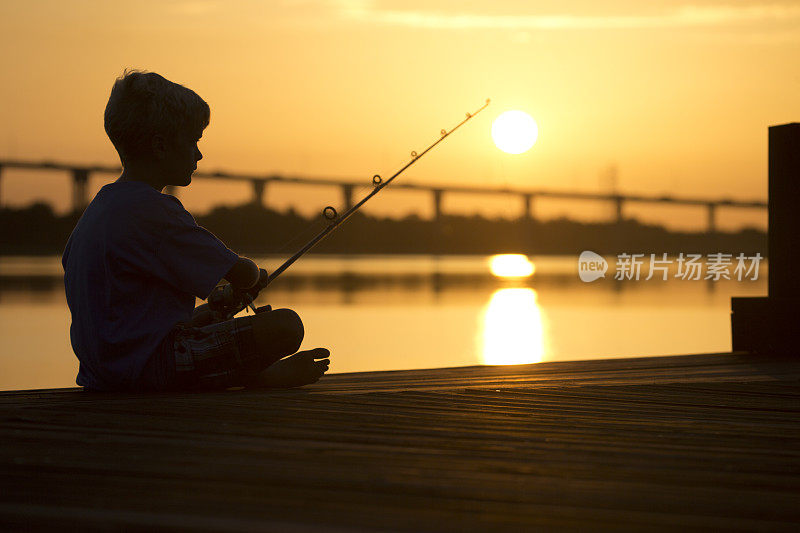 日出或日落，码头上的男孩在钓鱼