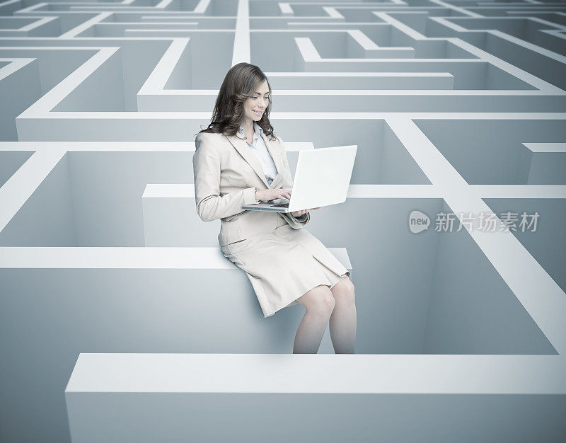 微笑的女商人坐在迷宫墙上用笔记本电脑
