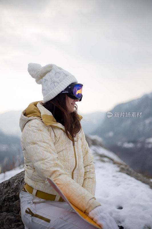 女人拿着滑雪板，背景是高山