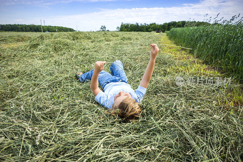 一个农场小孩躺在刚割下的干草地里