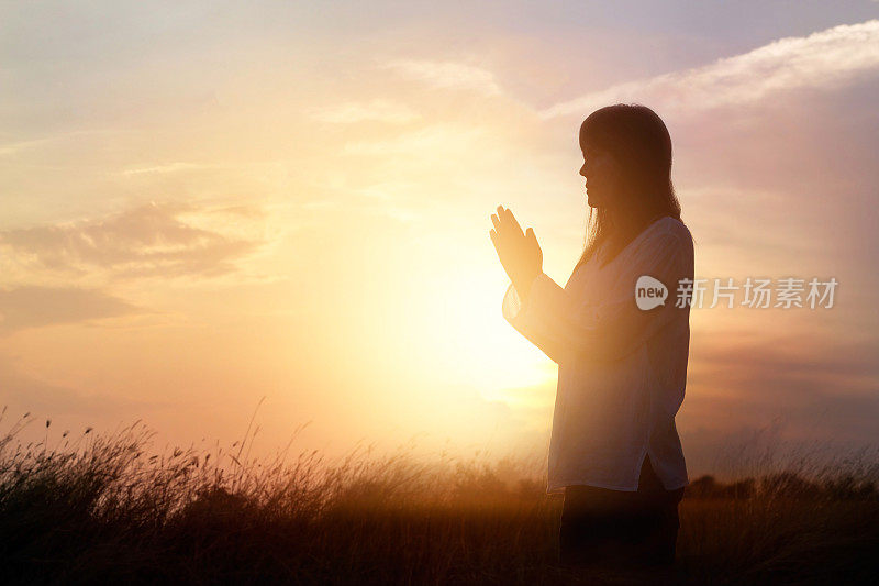 女人祈祷和练习冥想在自然日落背景，希望的概念