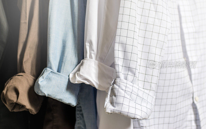 衣柜内部，展示折叠袖口和袖口的男士正装衬衫，白色，蓝色，棕色和黑色衬衫，浅色调和柔和的焦点