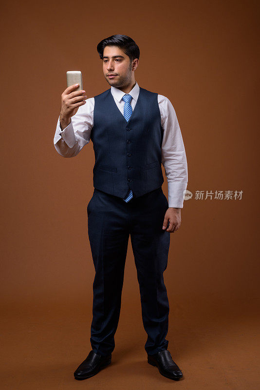 工作室拍摄的年轻英俊的伊朗商人在彩色背景下使用手机
