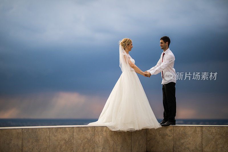 幸福的新娘和新郎一起站在露台的边缘，互相交谈