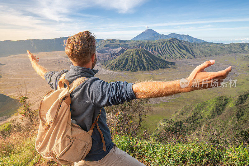 在印度尼西亚，年轻人徒步旅行，手臂伸开站在火山的山顶上，人们旅行的乐趣，冒险的概念，成功和成就