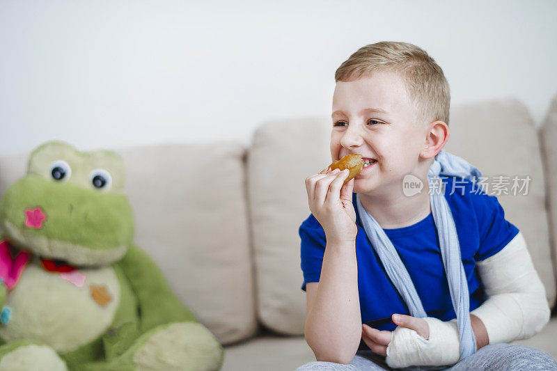 手臂骨折的微笑男孩在吃甜甜圈