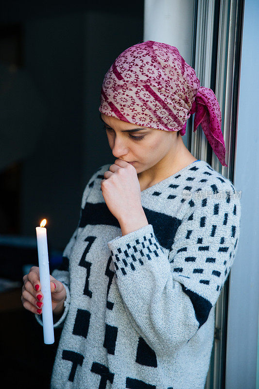 生病的女孩站在窗前，手里拿着一支蜡烛