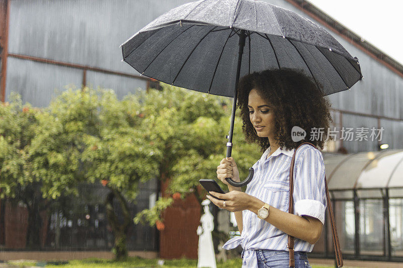 一名年轻女子在雨天用智能手机等出租车