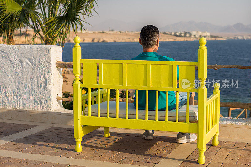 一名男子坐在彩色长凳上望着远方