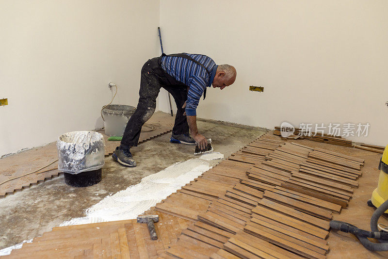 工作中的高级工人正在使用白色胶水安装层压地板或拼花地板