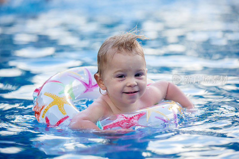 可爱的快乐的小男孩，蹒跚学步的男孩，有乐趣放松和玩在一个充气环游泳池在阳光明媚的日子在暑假
