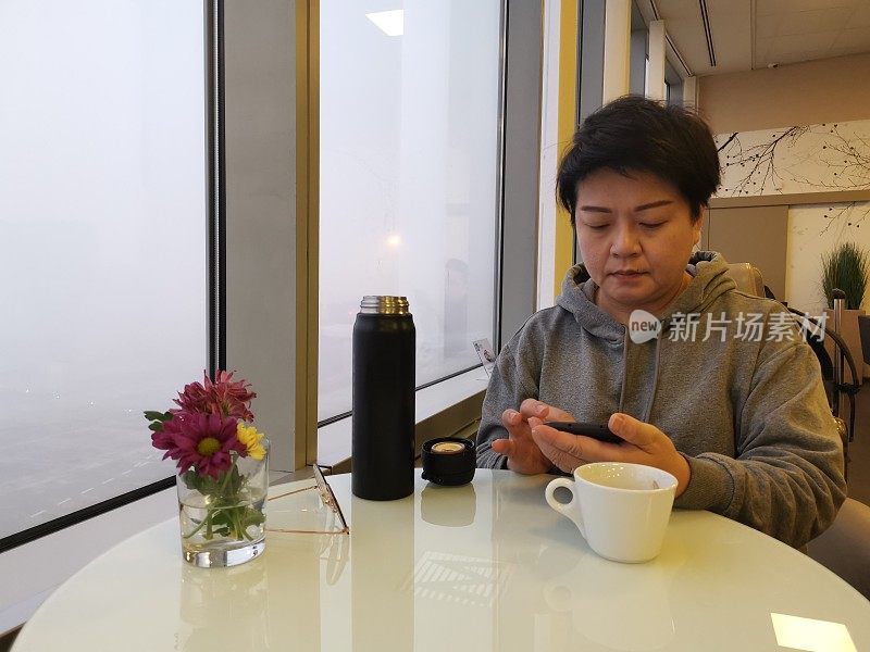 一名亚裔中国女游客在候机室候机时正看着自己的手机