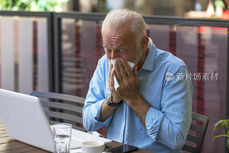 一个老人在餐厅花园用纸巾擤鼻子