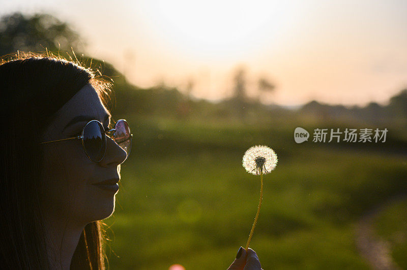 年轻的嬉皮女孩吹蒲公英在股票照片