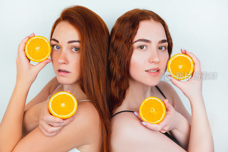 肖像两个红发妇女持有一半的橙色在他们的手站在他们的背转向孤立的白色背景，美丽的肖像概念