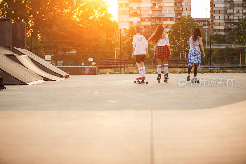 后视图三个十几岁的女朋友有乐趣和在滑板公园闲逛