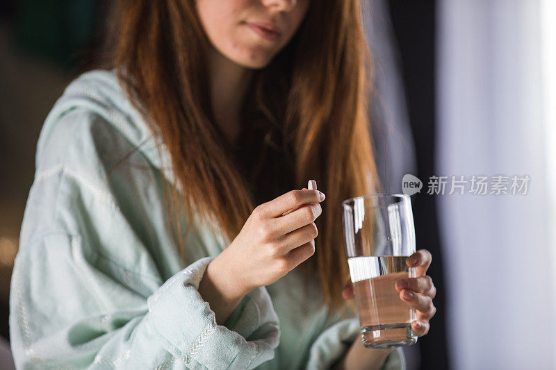 穿着浴袍的年轻女子拿着一粒药丸和一杯水