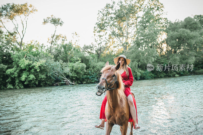 一个女人，穿着红色的裙子骑着她的马在河上