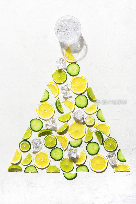 色彩鲜艳的图案由柑橘类水果，柠檬，酸橙和黄瓜片制成。杜松子酒装饰概念作为圣诞树与冰块和一杯杜松子酒在白色的背景