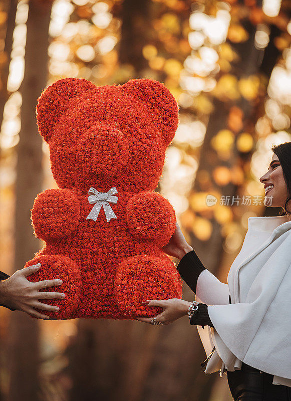 一个年轻人在户外把大泰迪熊作为礼物送给他的女朋友