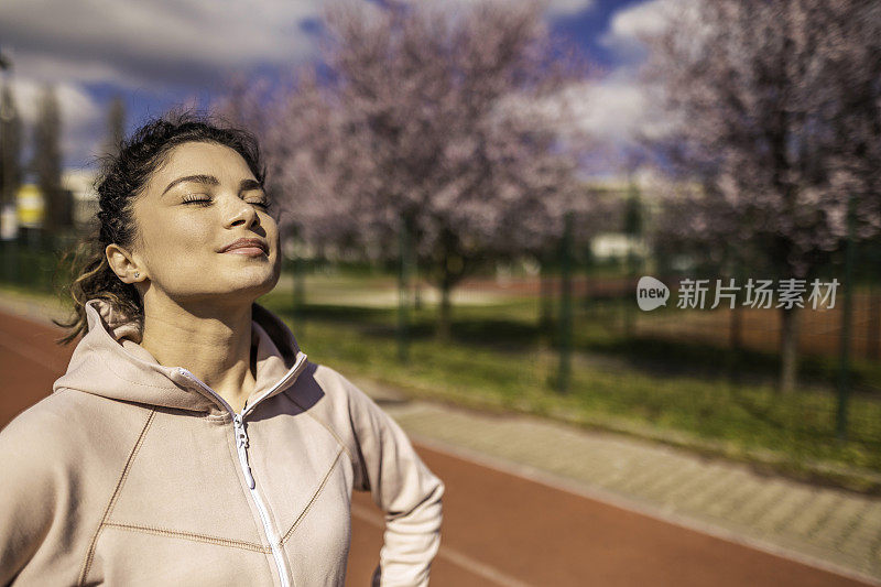 运动的年轻女子正在运动跑道上休息和做白日梦。