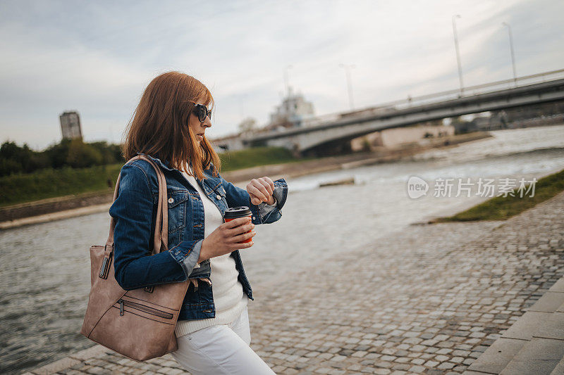 年轻女子在城市码头上用智能手机喝着外卖咖啡