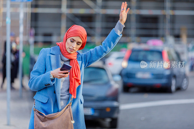 一名穆斯林妇女站在城市街道上试图搭车的肖像。