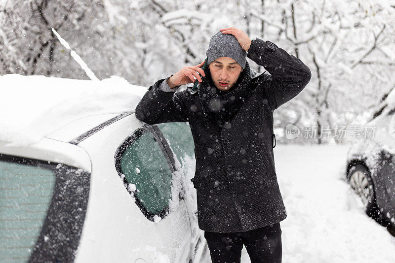 一个年轻人在雪地里，他的车坏了。冬天，一个男人站在一辆坏了的车上打电话给汽车服务公司