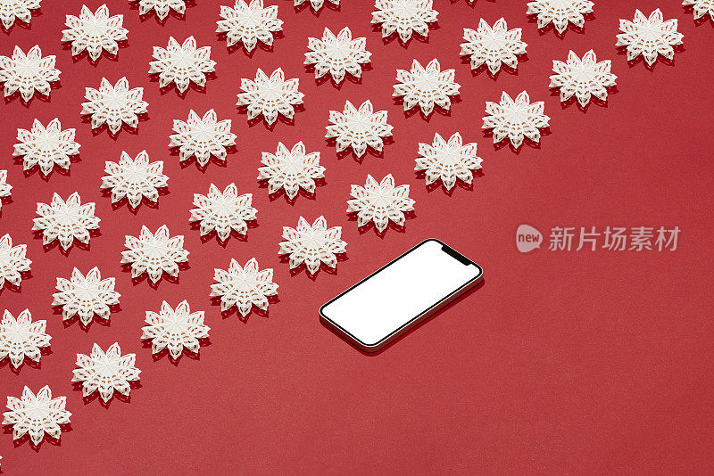 智能手机模型与白色雪花圣诞装饰平放在红色背景