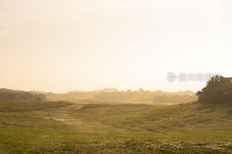 在一个阳光明媚的夏日清晨，沙丘上的薄雾笼罩着日出