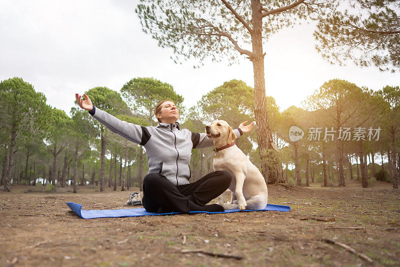 穿着运动服的成熟女人和她的狗在森林里冥想。