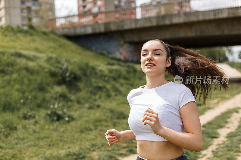 女孩在中午的阳光下在河边跑步。