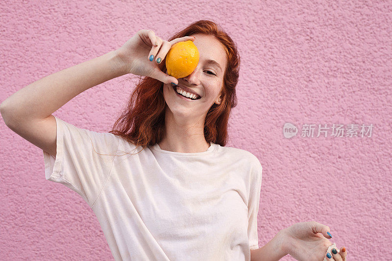 在粉色墙的背景下，一名女子把眼睛藏在橙色后面，在街上摆姿势