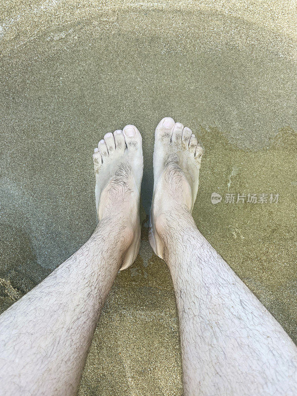 人的脚踩在沙滩上，男人的脚踩在水和沙上