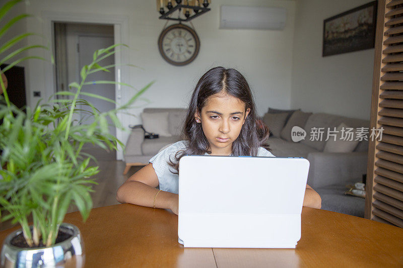 女孩坐在家里的桌子上做作业和使用数字平板电脑