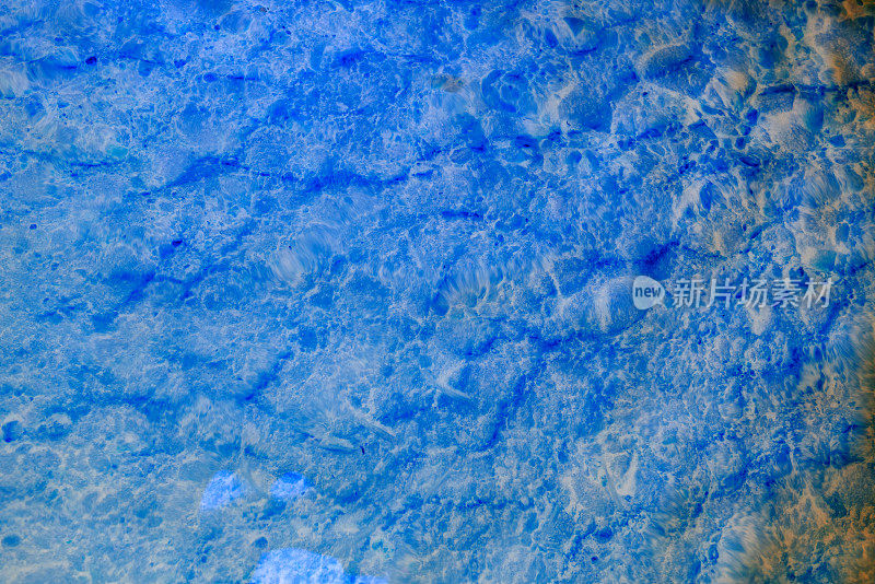 摘要照片辉光在霓虹灯蓝色的清水纹理与光反射与波浪和沙质底部。背景是自然的。