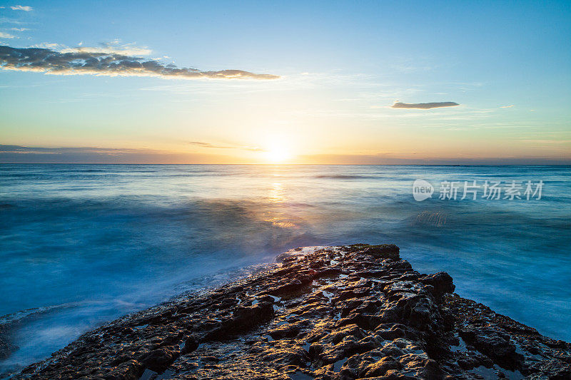 海面上明亮的日出，海浪冲刷着岩石