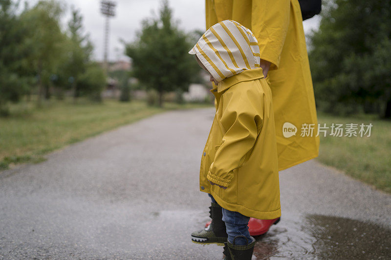 母亲和一个孩子。穿着雨衣的母子在公园里手牵着手