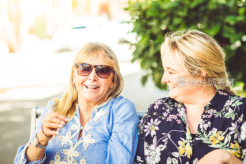 两个快乐大笑的成年女性，母亲和女儿，戴着太阳镜在户外一起欢笑