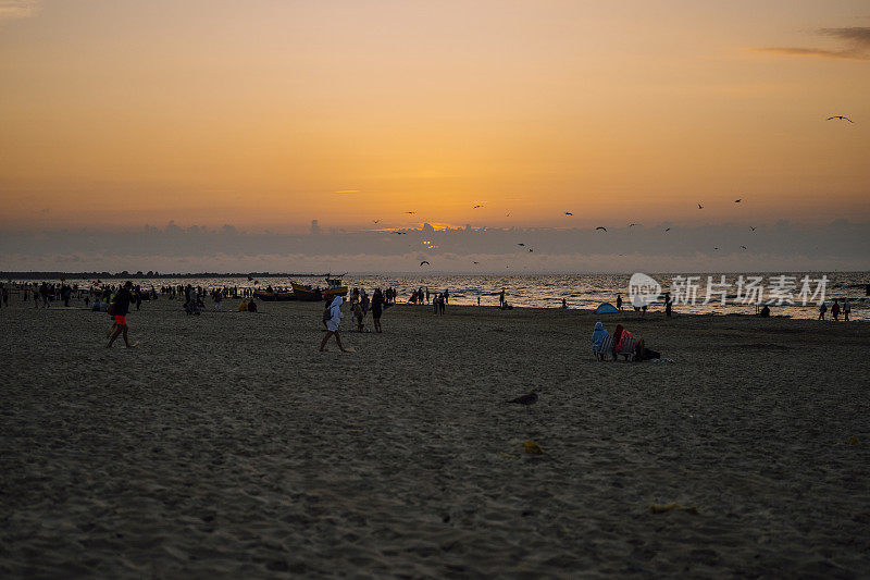 金色的天空和海上的夕阳。人们在沙滩上散步