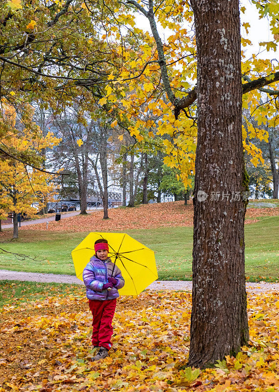 孩子，白人女孩，8岁，秋天散步。一个孩子站在秋天的公园里，拿着一把明黄色的伞，微笑着。