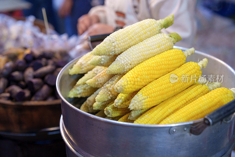 一个特写镜头，在一个亚洲夜市，一个金属蒸笼托盘上的蒸玉米，准备出售食物。